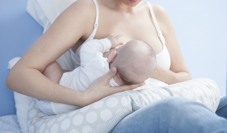 Young mother feeding breast. She is using a nursing pillow with the baby on side